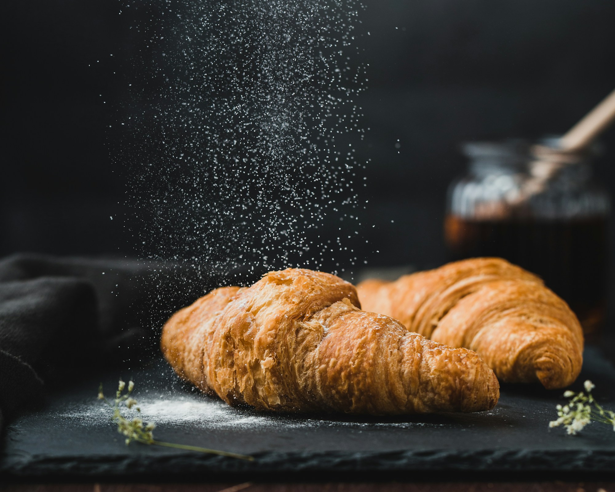 Fresh croissants dusted with powdered sugar on a dark slate board.